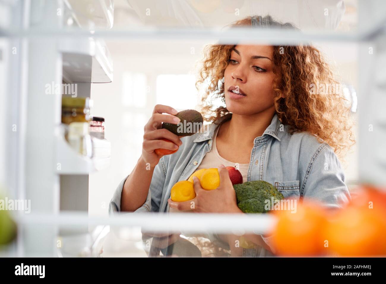Vista dall'interno del frigorifero come donna apre la porta e pacchi cibo su ripiani Foto Stock