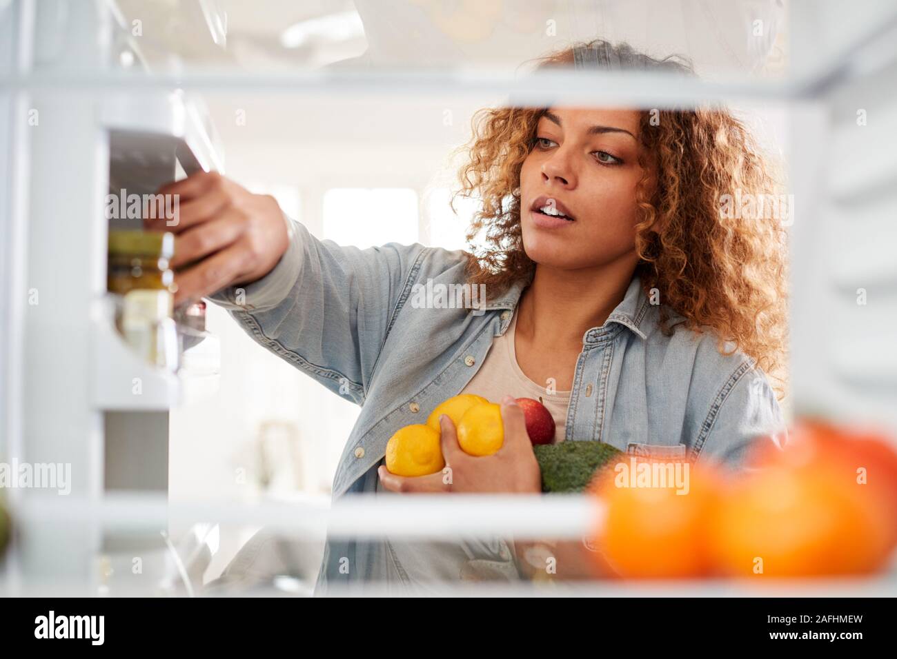 Vista dall'interno del frigorifero come donna apre la porta e pacchi cibo su ripiani Foto Stock