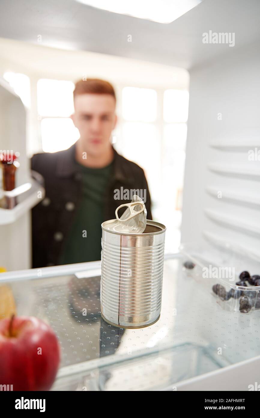 Giovane uomo cerca all'interno del frigorifero vuoto tranne che per aprire il barattolo di latta sul ripiano Foto Stock