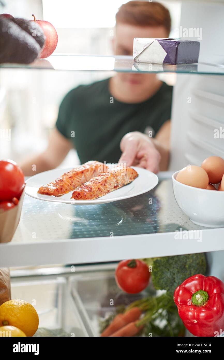 Giovane uomo di raggiungere all'interno del frigorifero di un alimento sano per il salmone fresco su piastra Foto Stock
