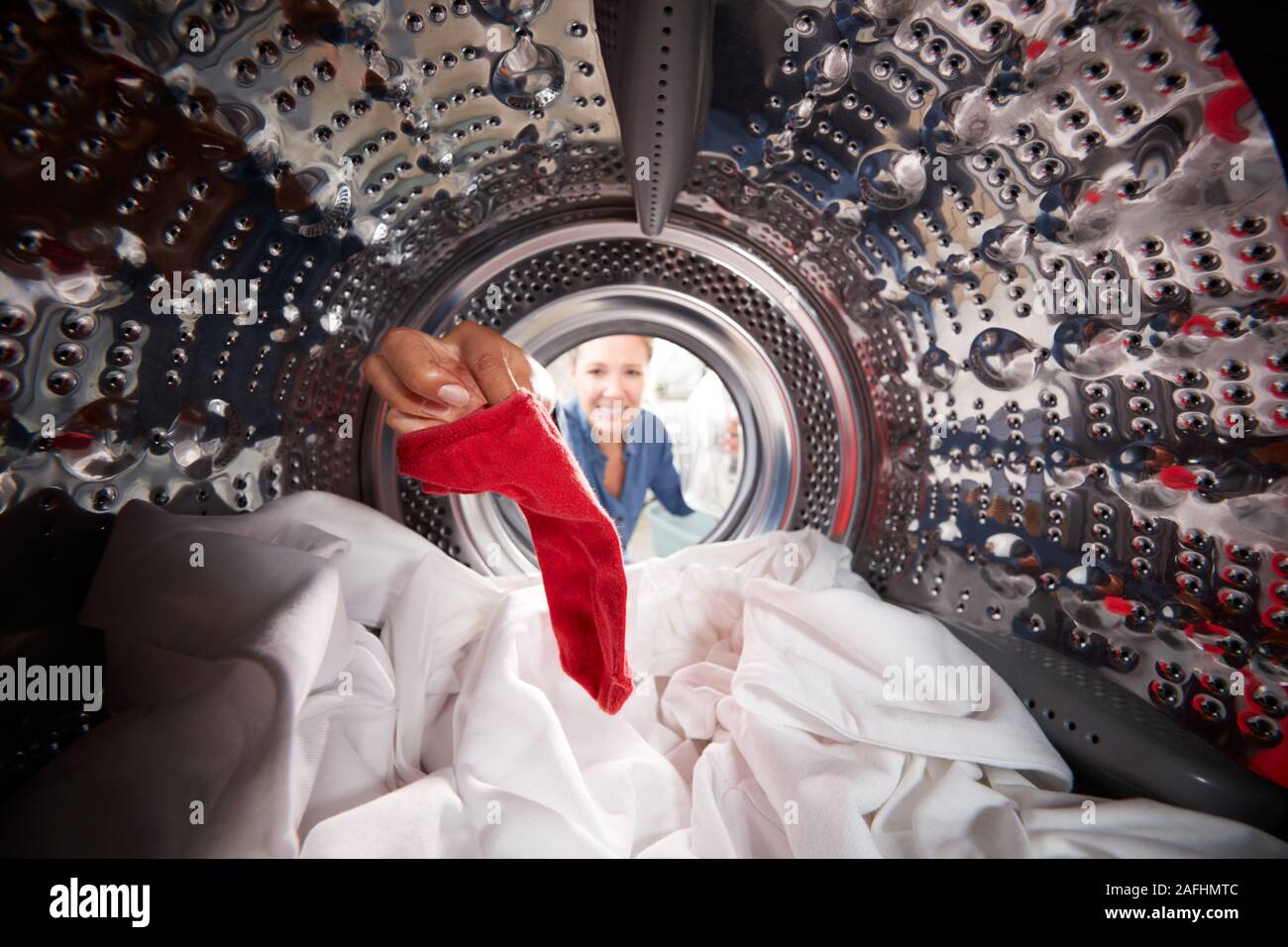 Donna tenendo fuori calza rossa mescolato con il bianco biancheria dalla macchina di lavaggio Foto Stock