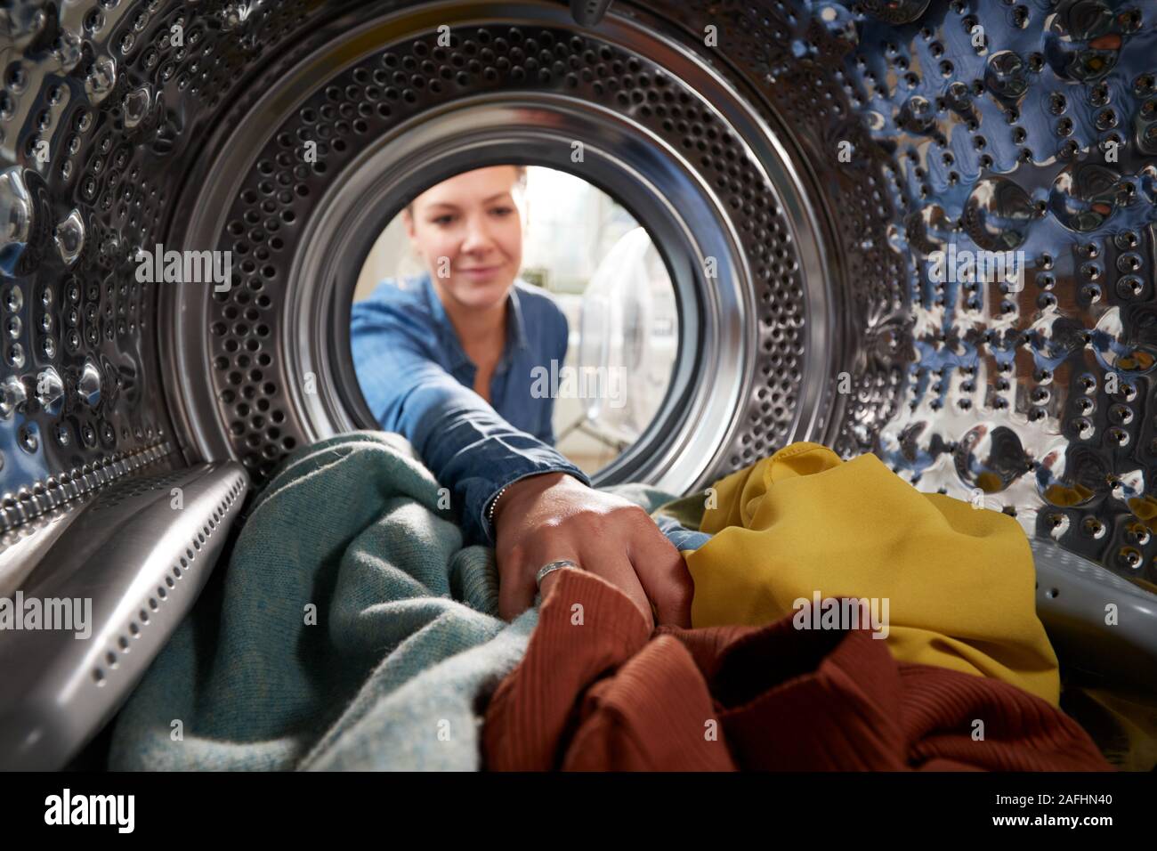 Vista dall'interno della macchina di lavaggio come giovane donna fa servizio lavanderia Foto Stock