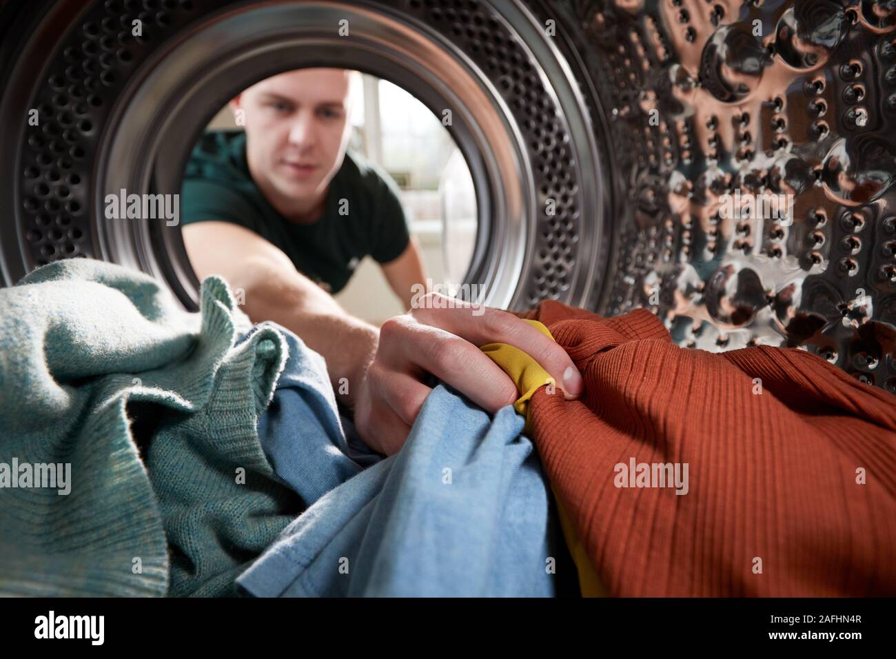 Vista dall'interno della macchina di lavaggio come giovane uomo fa servizio lavanderia Foto Stock