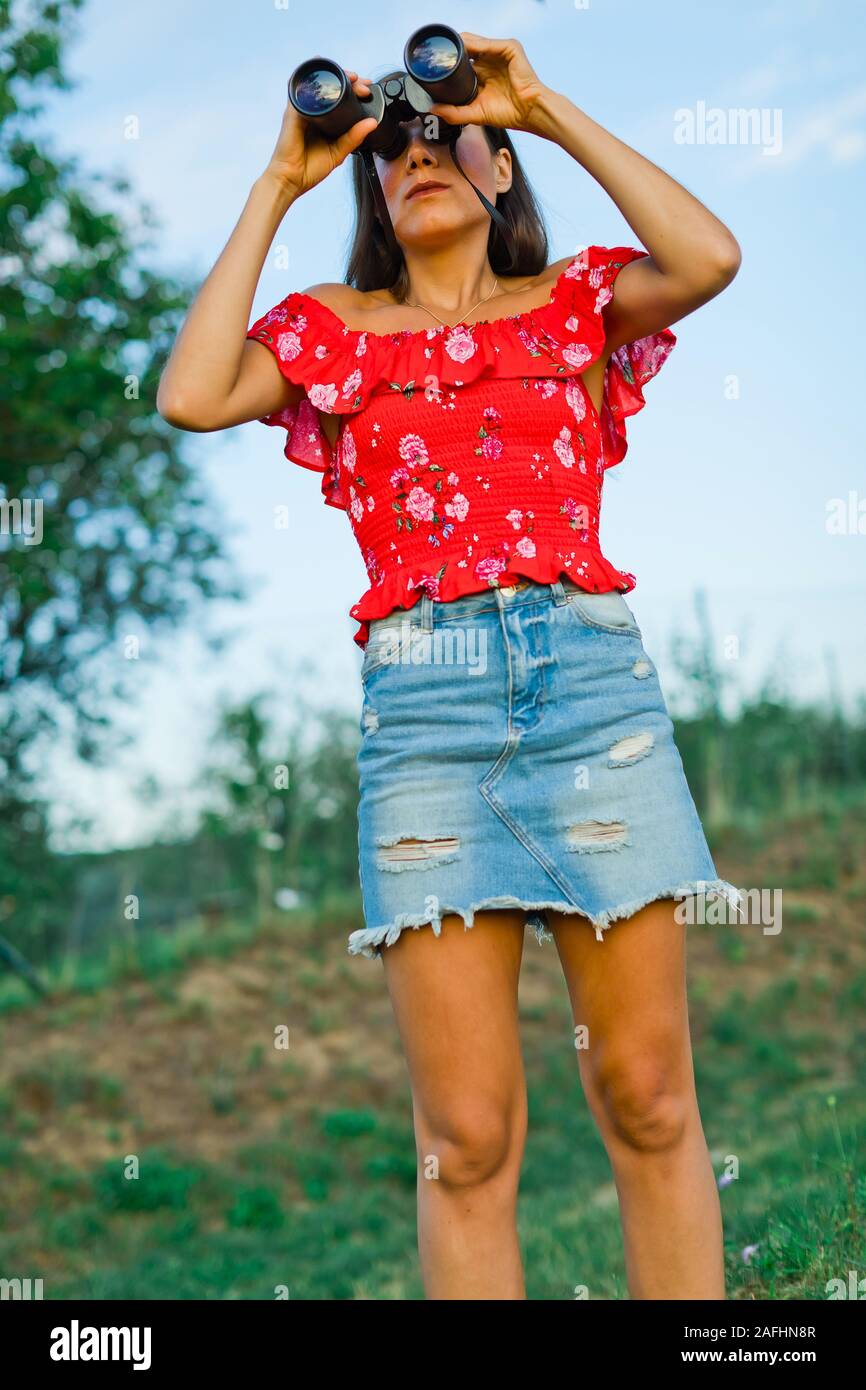 Donna in abito rosso e breve gonna jeans guardando attraverso il binocolo  Foto stock - Alamy