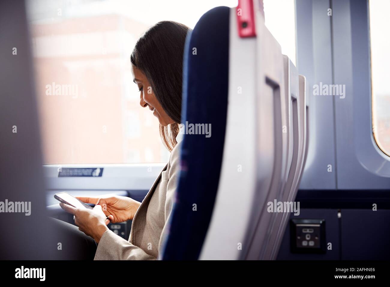 Imprenditrice seduta in treno il pendolarismo di lavoro controllare i messaggi sul telefono cellulare Foto Stock