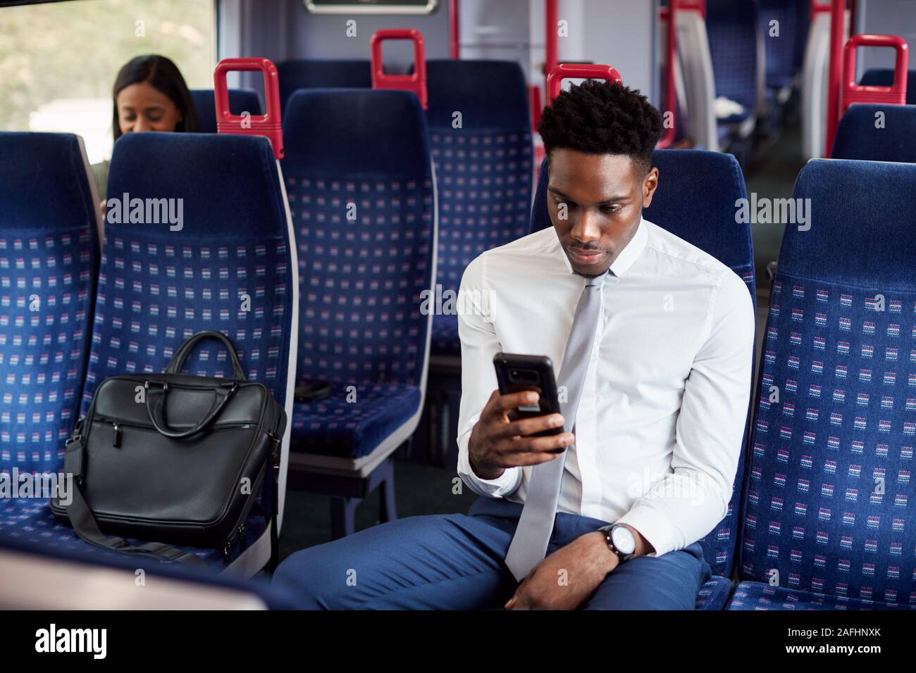 Imprenditore seduto in treno il pendolarismo di lavoro controllare i messaggi sul telefono cellulare Foto Stock