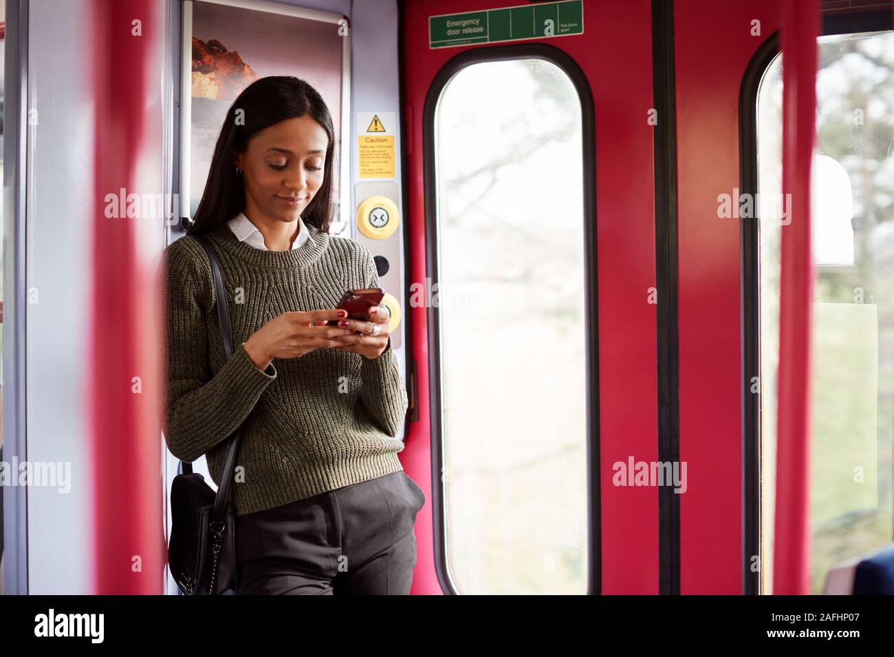 Femmina in piedi passeggero da porte In treno guardando al telefono cellulare Foto Stock