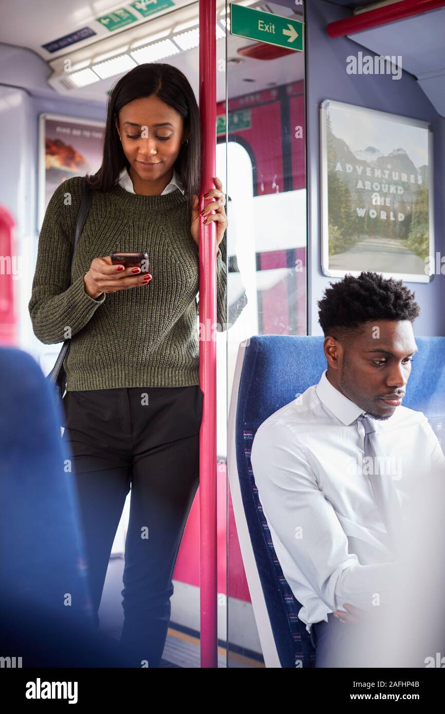 Femmina in piedi passeggero da porte In treno guardando al telefono cellulare Foto Stock