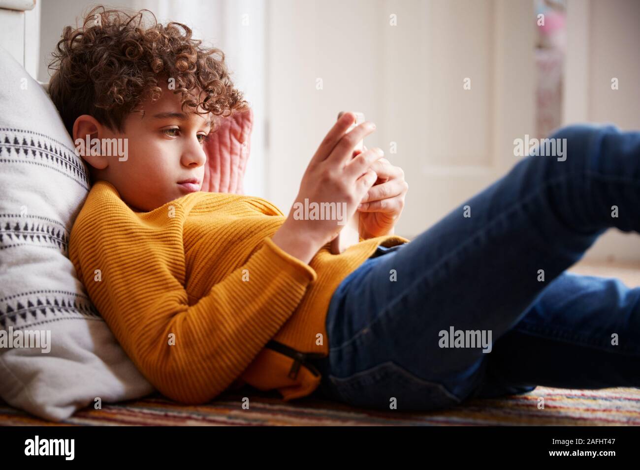 Ragazzo disteso sul pavimento della camera da letto di passare troppo tempo utilizzando il telefono cellulare Foto Stock