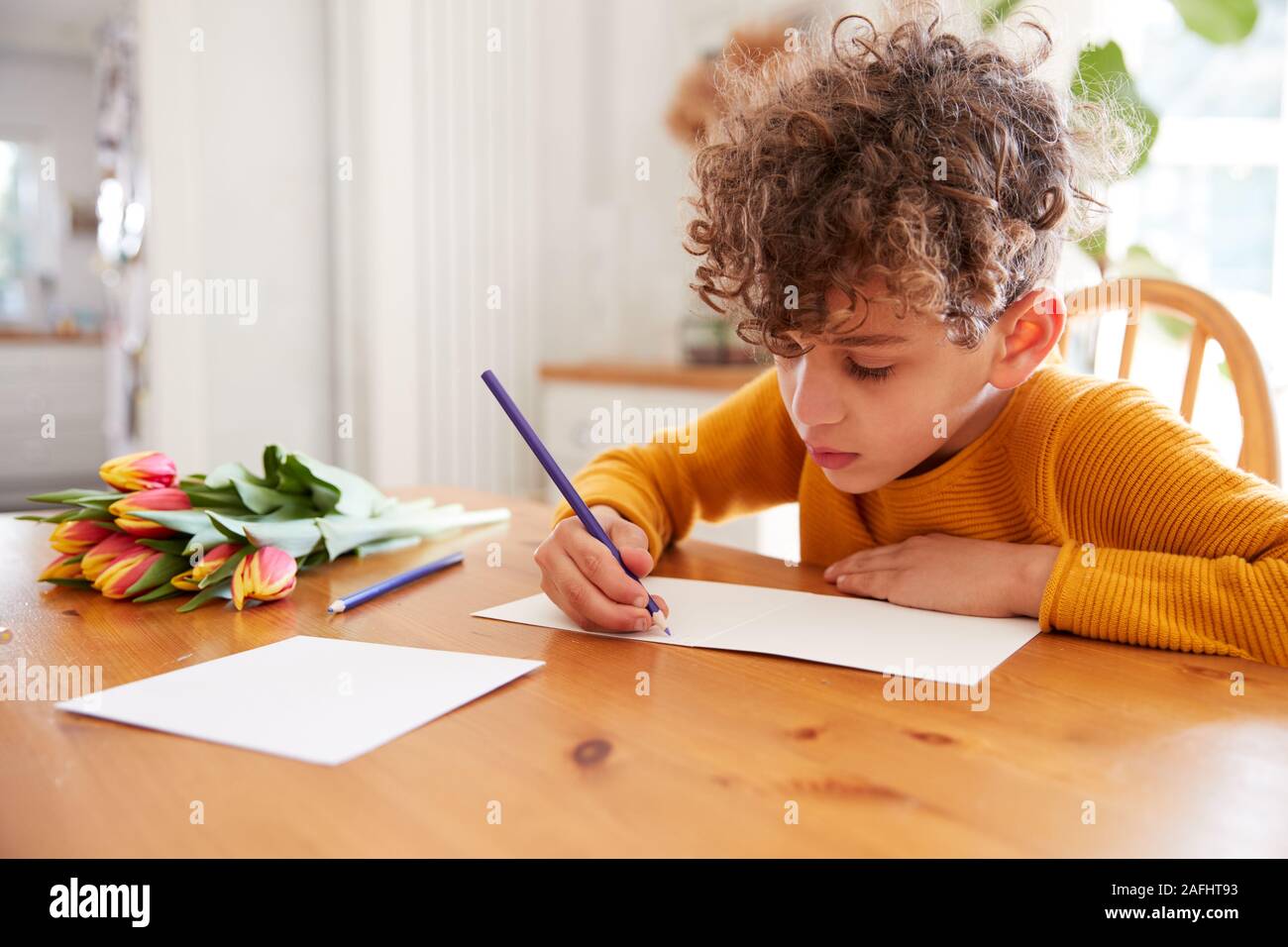 Ragazzo giovane a casa con il mazzo di fiori la scrittura in madri di giorno della carta Foto Stock