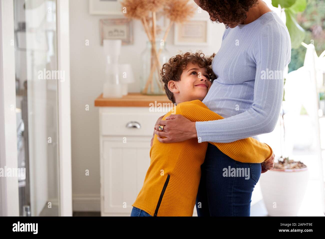 Amare il figlio dando madre abbraccio al chiuso in casa Foto Stock