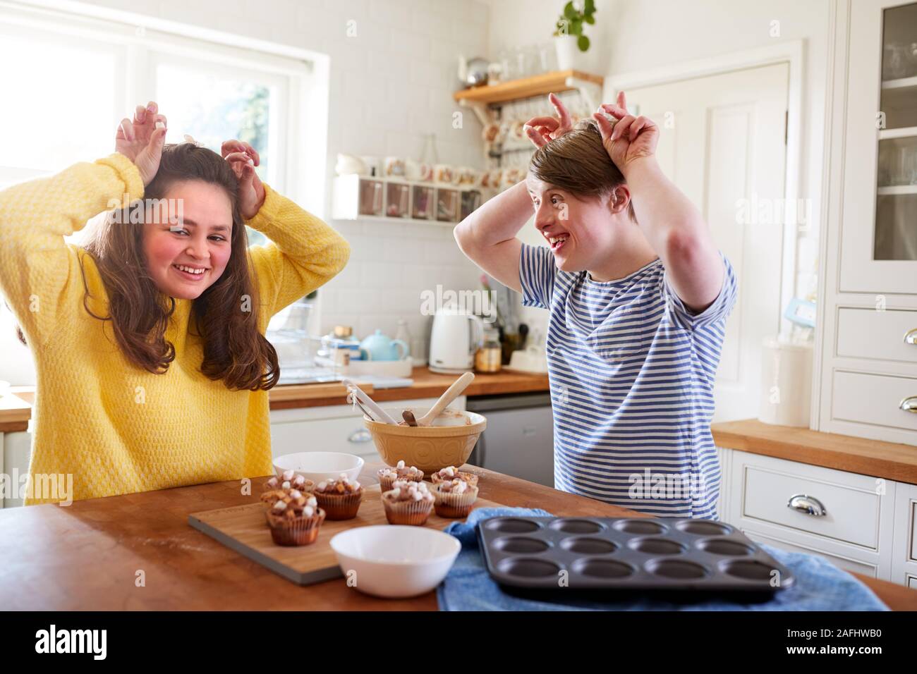 Giovani sindrome Downs giovane decorazione tortini fatti in casa con Marshmallows in cucina a casa Foto Stock