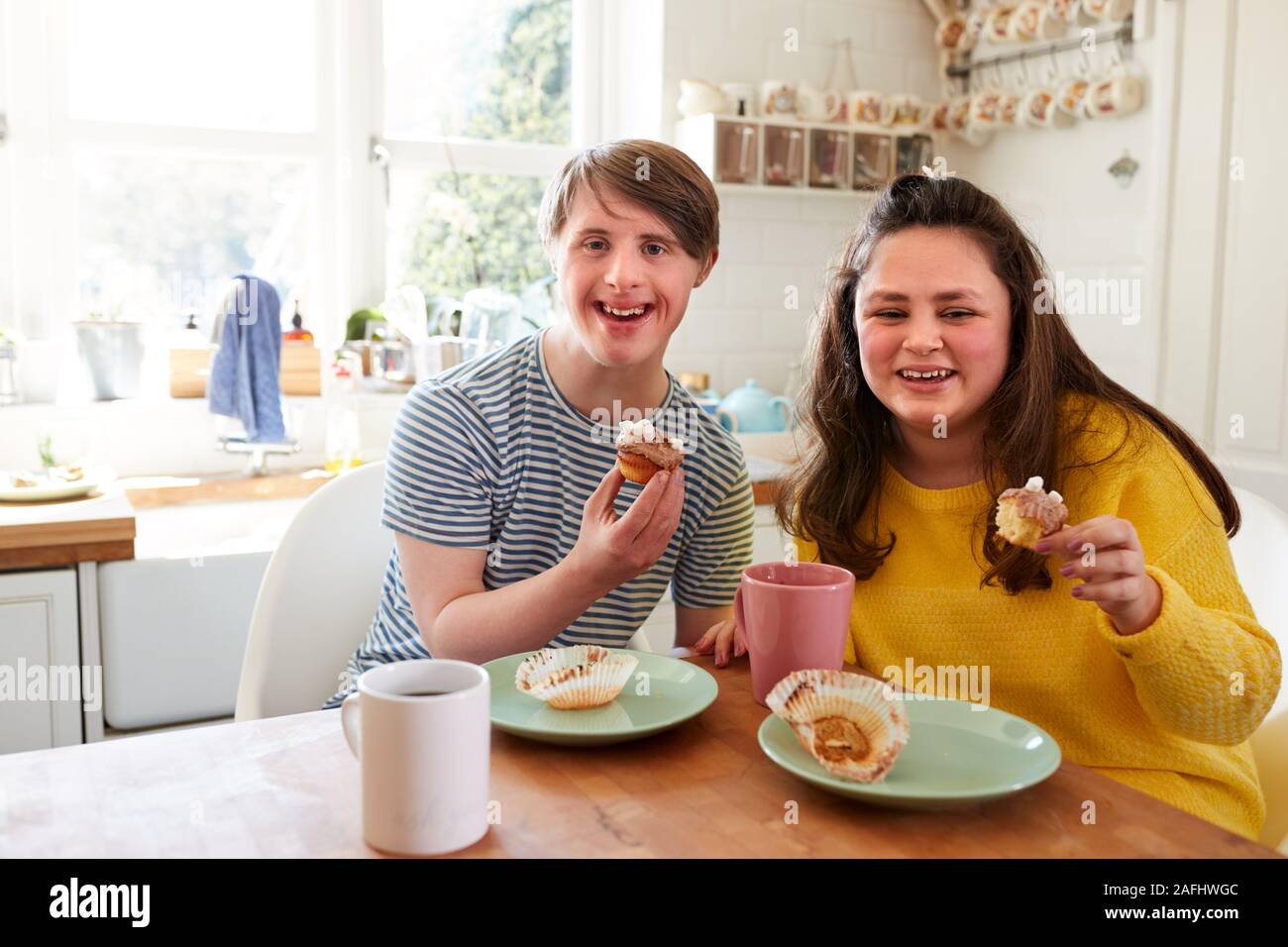Ritratto di giovane sindrome Downs giovane godendo di tè e una fetta di torta in cucina a casa Foto Stock