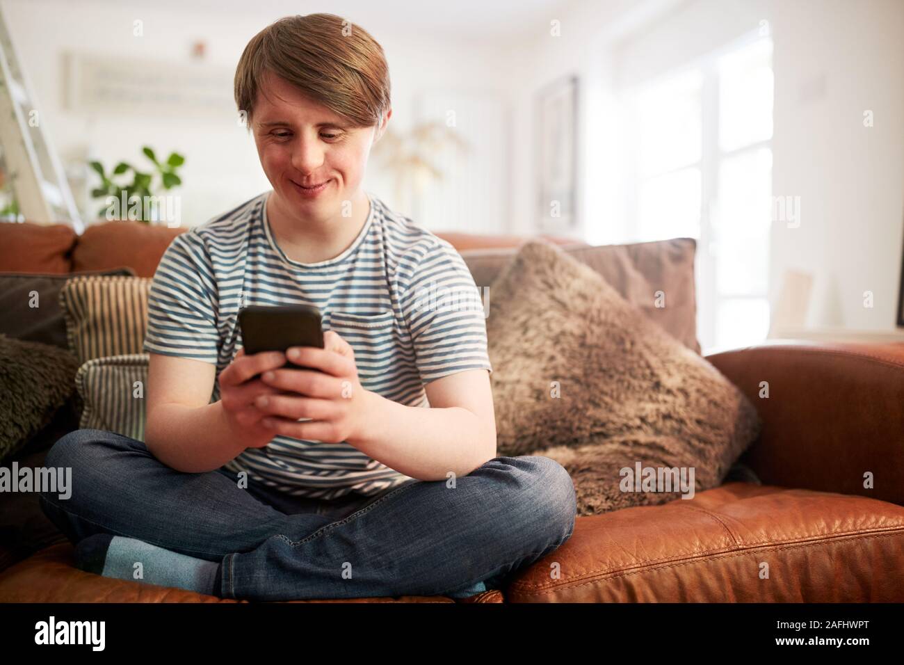 Giovani la sindrome di Down uomo seduto sul divano utilizzando il telefono cellulare a casa Foto Stock