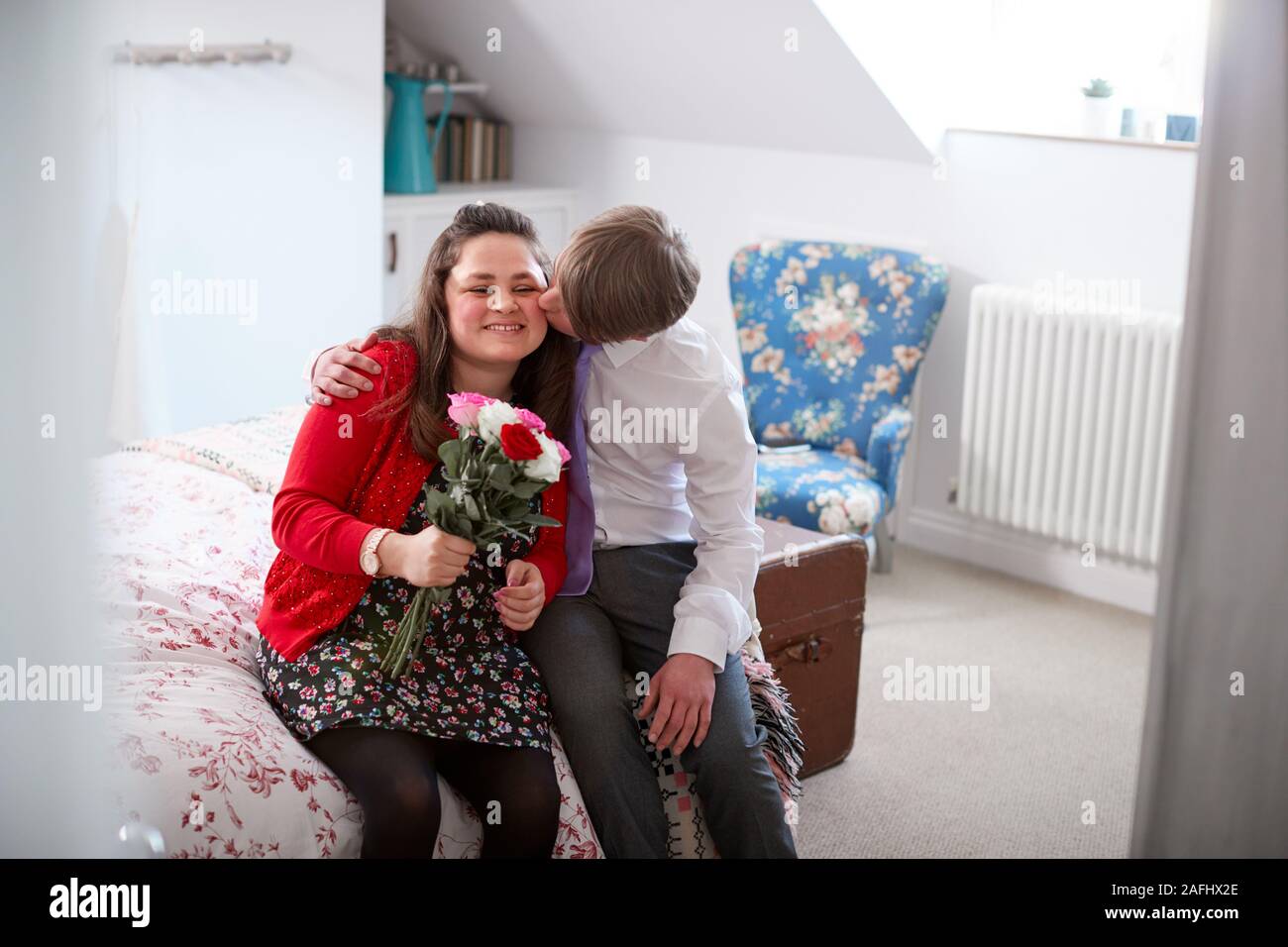 Amare i giovani la sindrome di Downs giovane seduto sul letto con Uomo Donna dando fiori Foto Stock