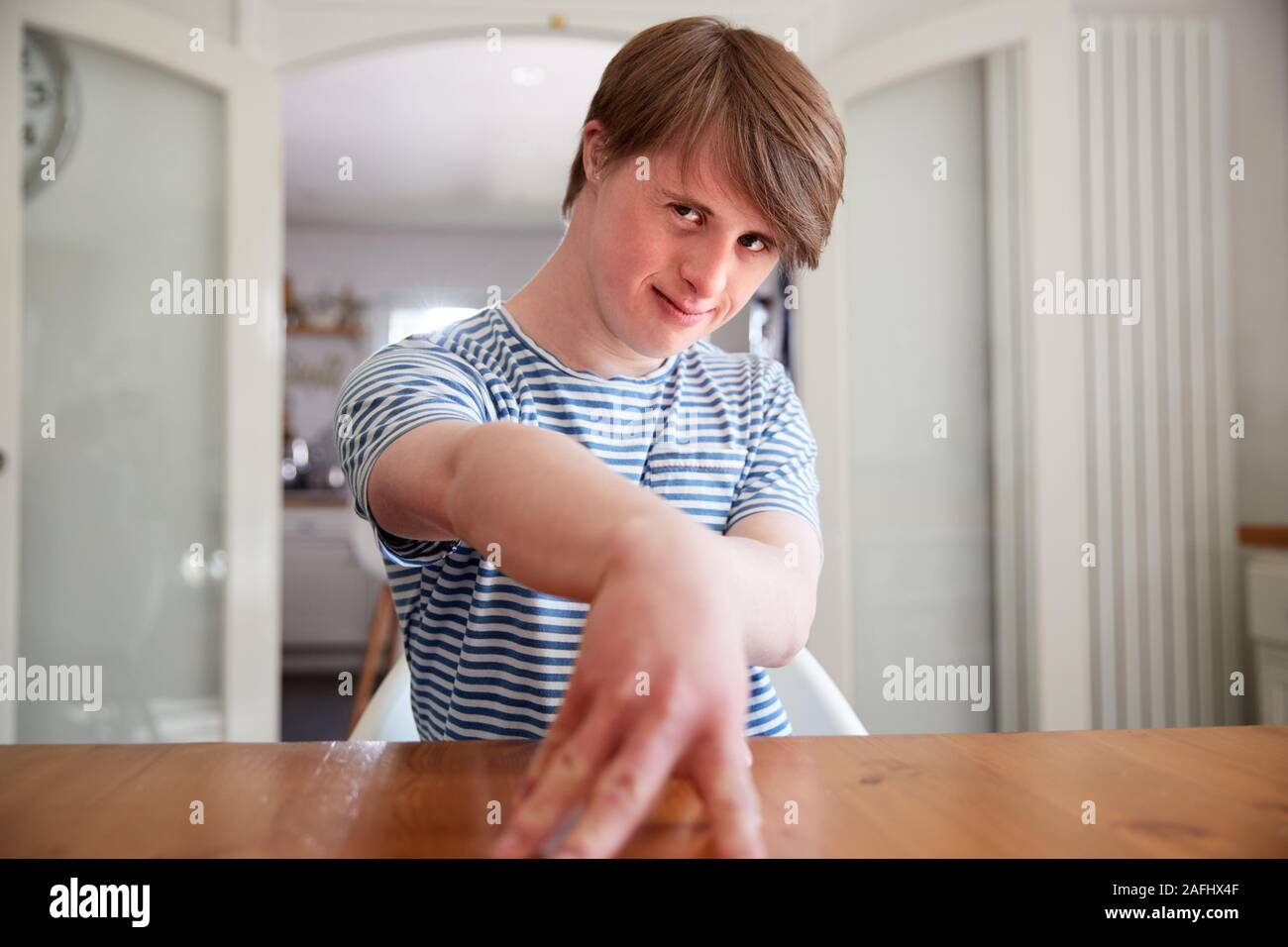 Ritratto di giovane sindrome Downs uomo seduto a tavola in cucina Foto Stock
