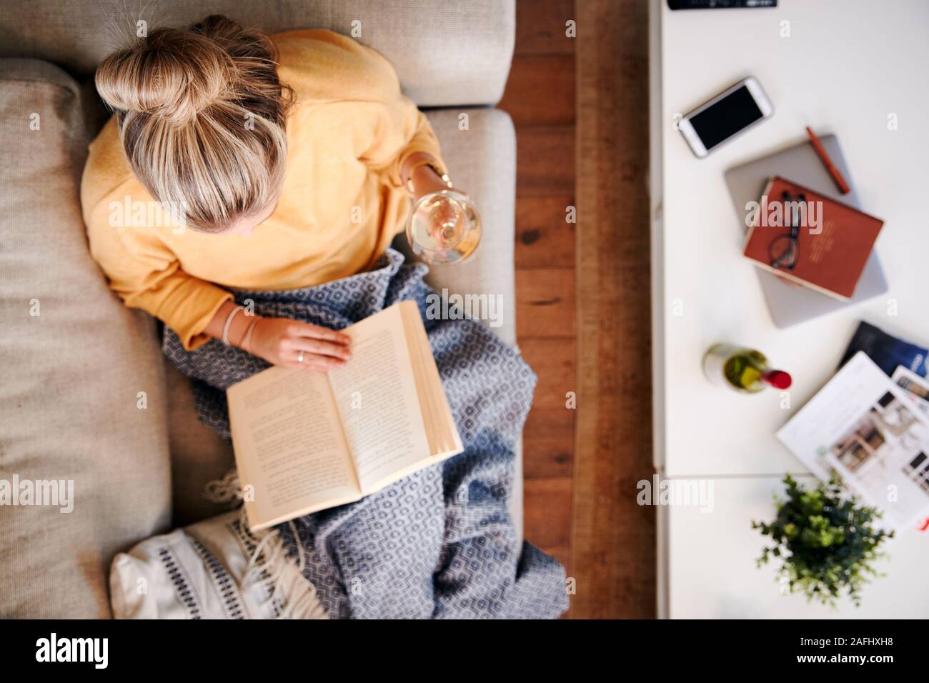 Scatto dall'alto guardando verso il basso sulla donna a casa sdraiato sul libro di lettura e di bere il vino Foto Stock