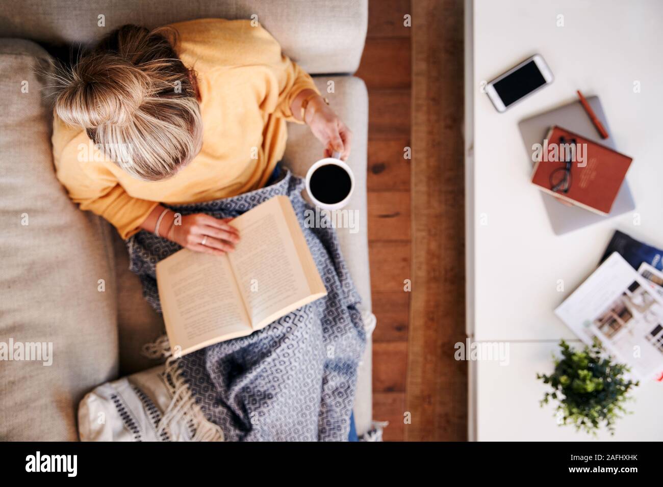 Scatto dall'alto guardando verso il basso sulla donna a casa sdraiato sul libro di lettura e di bere il caffè Foto Stock