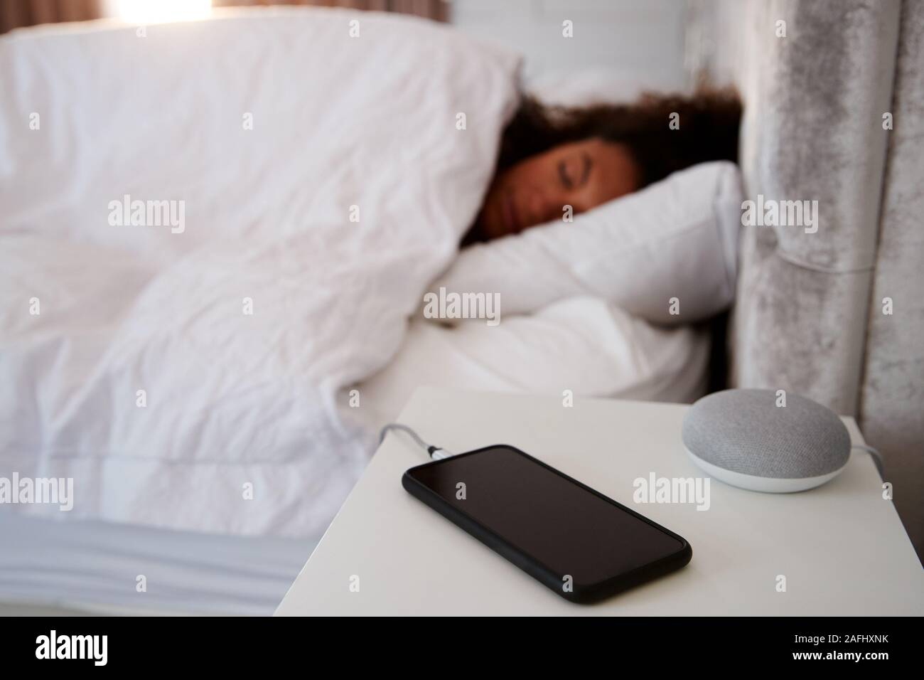 La donna dorme nel letto con telefono mobile e Assistente vocale sul comodino Foto Stock