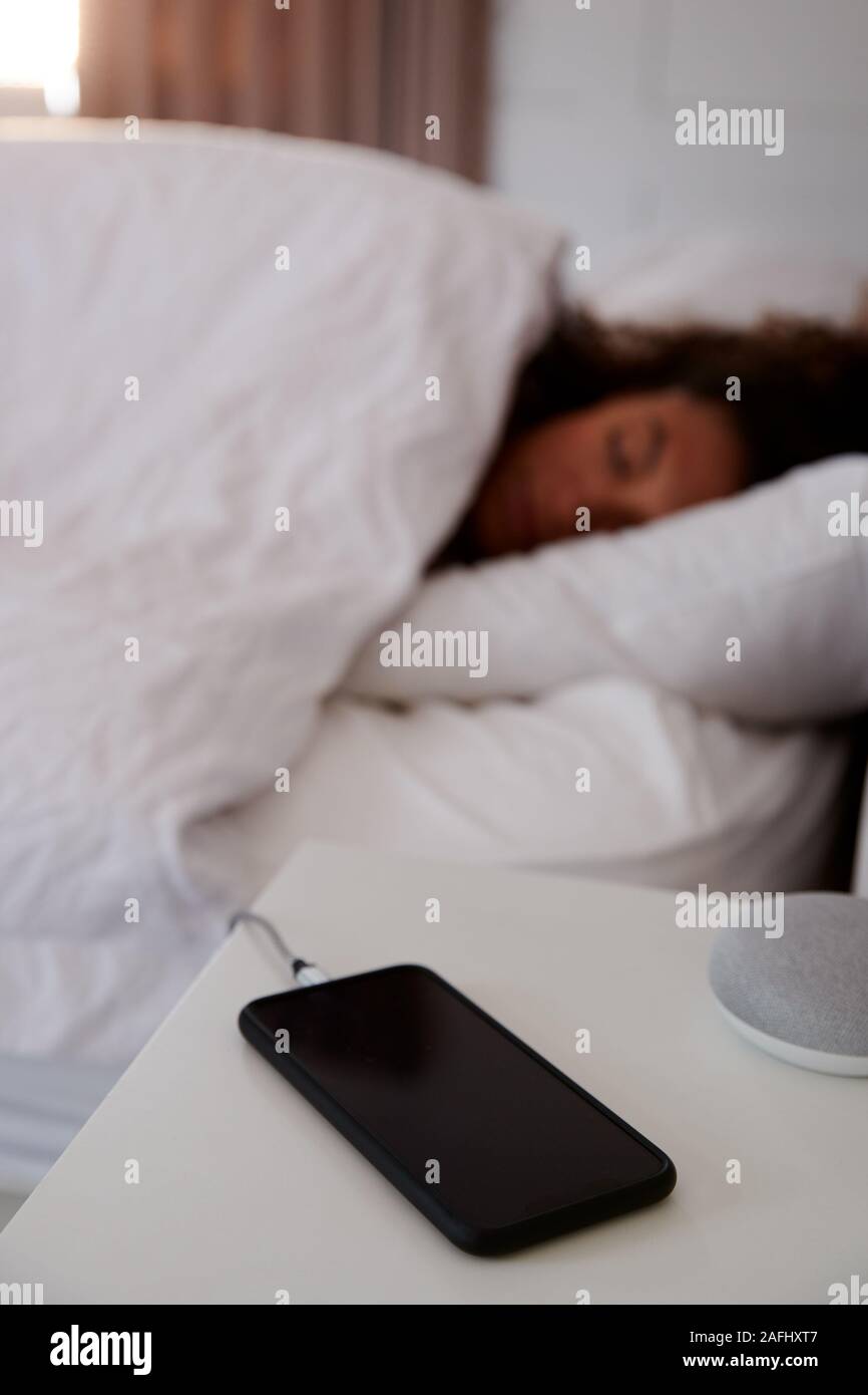La donna dorme nel letto con telefono cellulare sul comodino Foto Stock