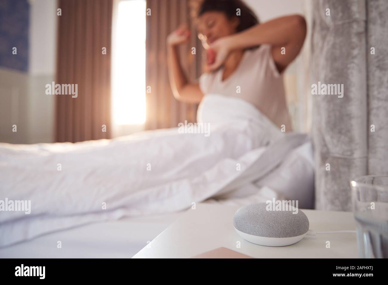 Donna di svegliarvi in letto con Assistente vocale sul comodino accanto a lei Foto Stock