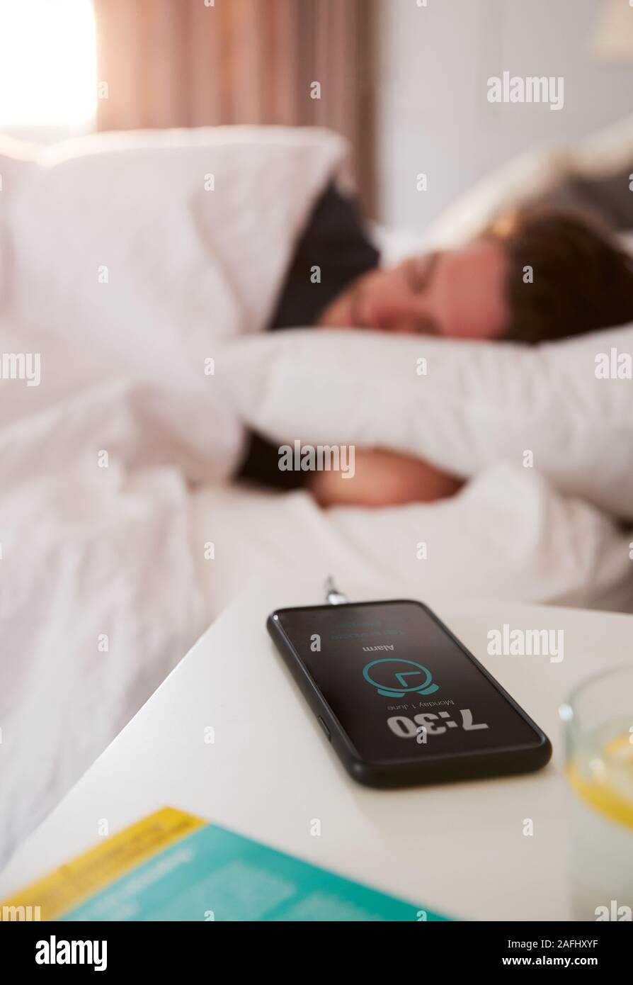 Uomo dorme nel letto con telefono cellulare sul comodino Foto Stock
