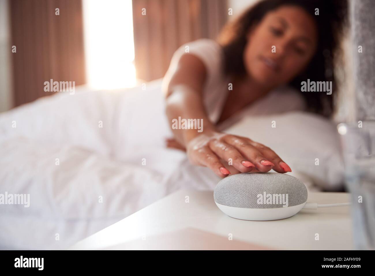 Donna di svegliarvi in letto con Assistente vocale sul comodino accanto a lei Foto Stock
