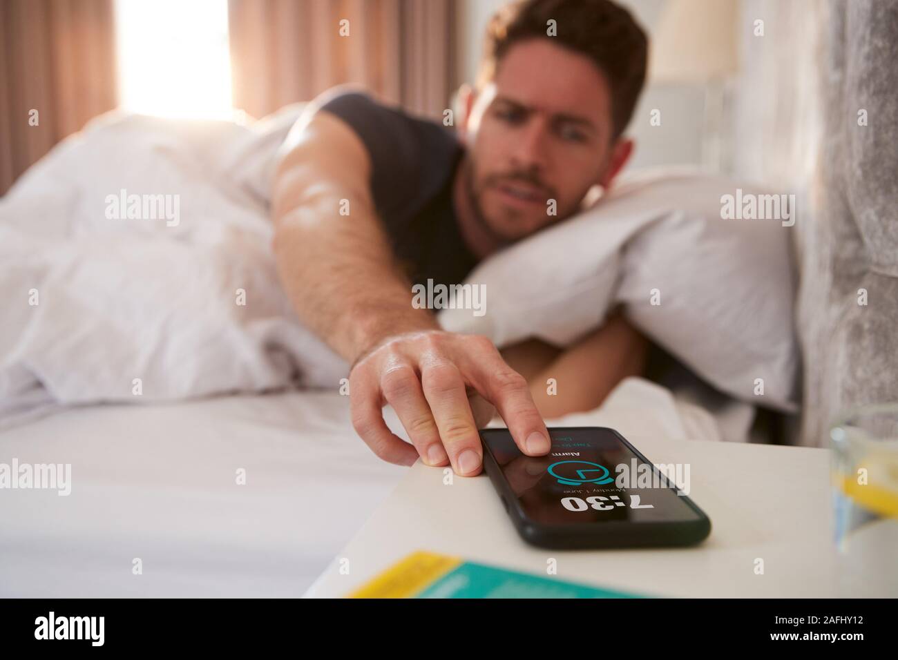 Uomo di svegliarvi in Bed raggiunge fuori per disattivare la sveglia sul telefono cellulare Foto Stock