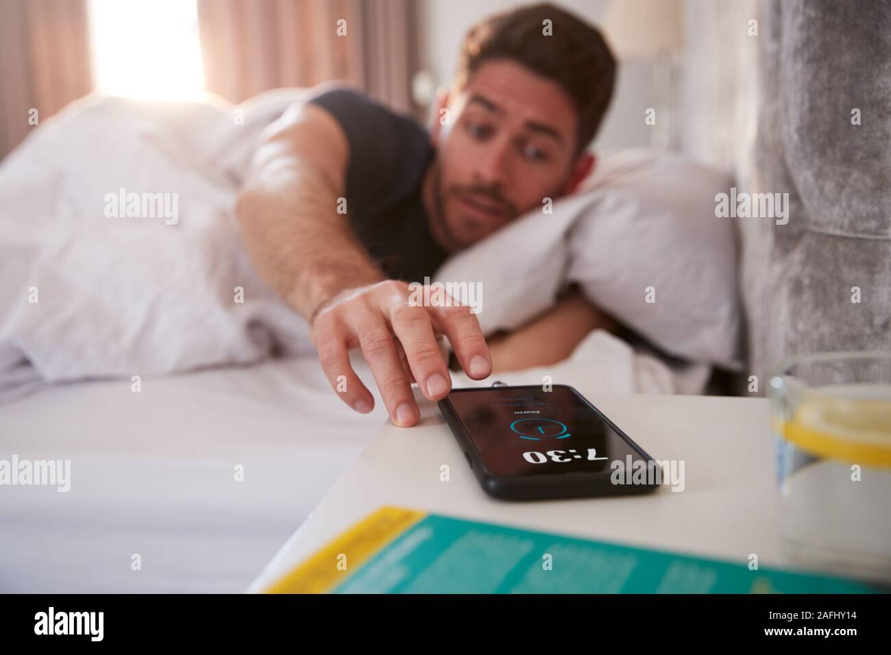 Uomo di svegliarvi in Bed raggiunge fuori per disattivare la sveglia sul telefono cellulare Foto Stock