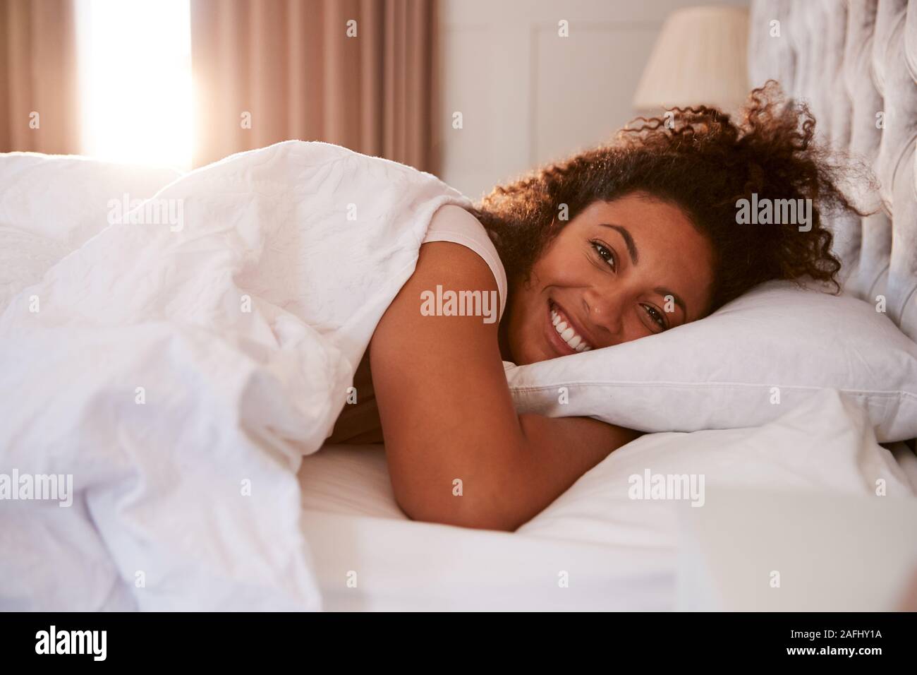 Ritratto di donna svegliarsi nel letto e sorridente in telecamera Foto Stock