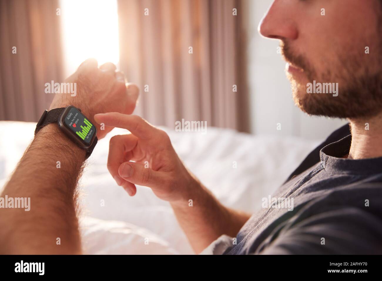 Uomo seduto a letto guardando lo schermo di Smart Watch Foto Stock