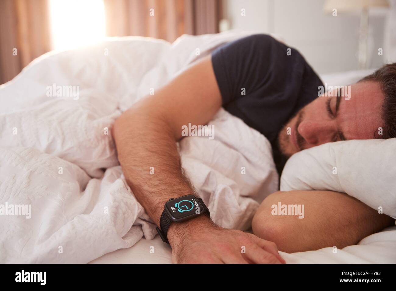 L'uomo addormentato nel letto indossando Smart guarda come Sun si rompe attraverso le tende Foto Stock