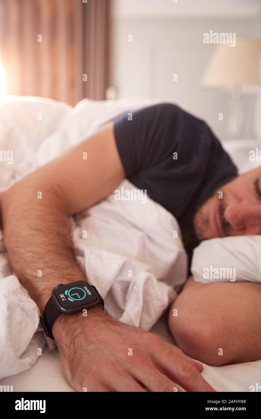 L'uomo addormentato nel letto indossando Smart guarda come Sun si rompe attraverso le tende Foto Stock
