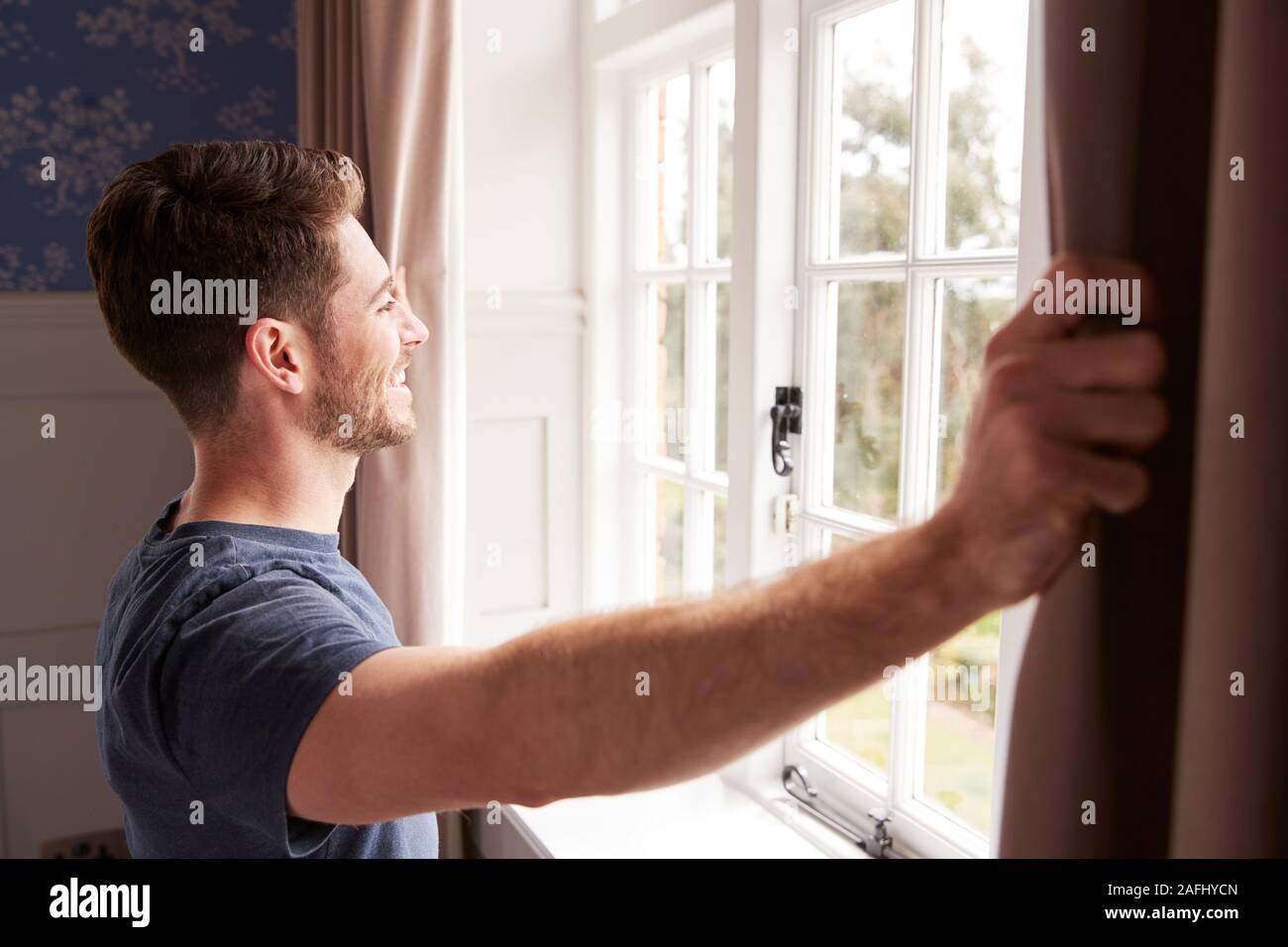 Uomo che indossa pigiama apertura camera da letto tende all inizio di un nuovo giorno Foto Stock