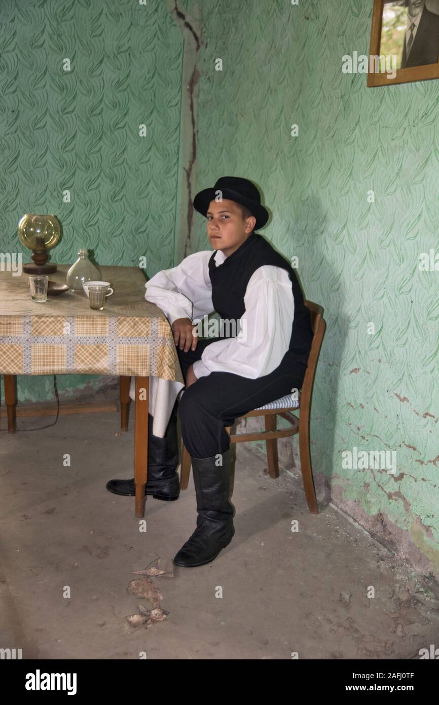 Ivanovo, Serbia, 15 aprile 2018. Un ragazzo solitario con un cappello è seduto da solo a un tavolo in una stanza e pensare la sua vita. La camera anche crollata wi Foto Stock