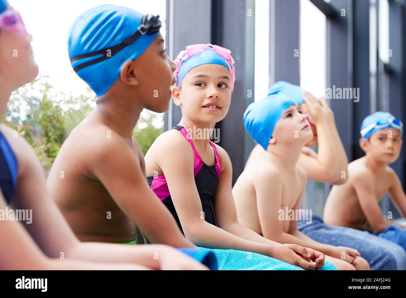 Un gruppo di bambini seduti sul bordo della piscina in attesa per la lezione di nuoto Foto Stock