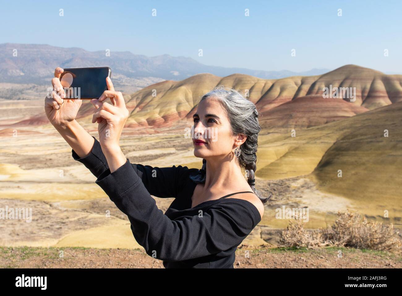 Un giovane brunette con trefoli grigio prende selfies a colline dipinte si affacciano Foto Stock