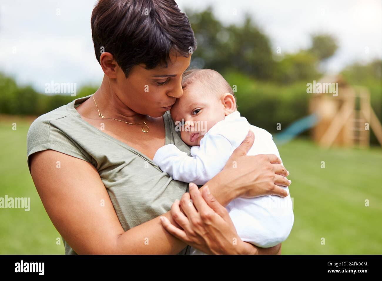 Amorevole Madre Holding e baciare 3 Mesi figlia del bambino nel giardino di casa Foto Stock