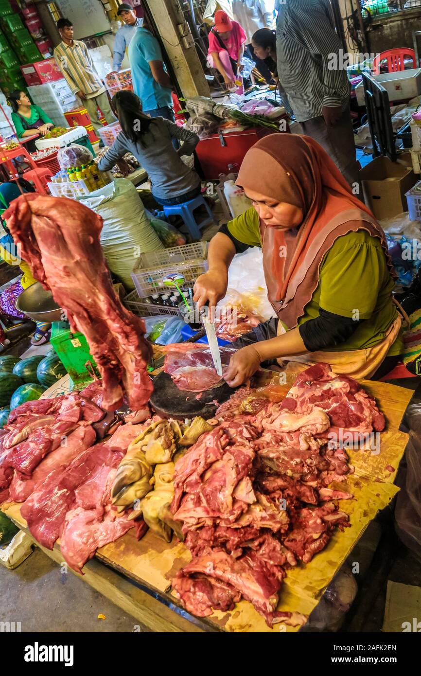 Donna che taglia la carne in una stalla nel mercato centrale occupato in questa vecchia città coloniale francese porto fiume; Kambot, Cambogia Foto Stock