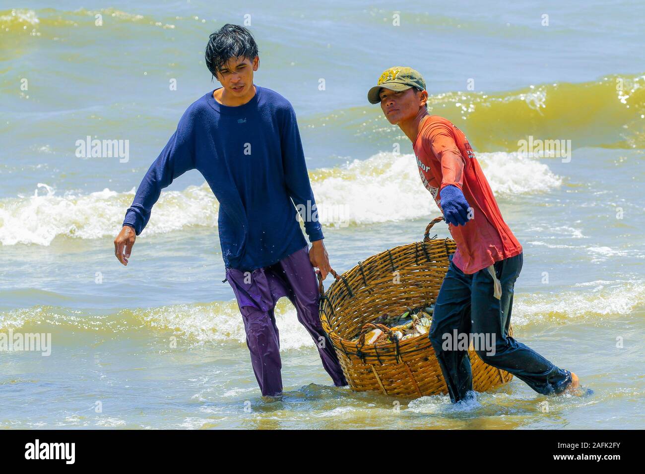 I pescatori trascina un cesto di pesci più piccoli da loro catture in questo tranquillo il francese ex località di villeggiatura, conosciuto per i suoi piatti di pesce; Kep, Kep Provincia, Cambogia Foto Stock