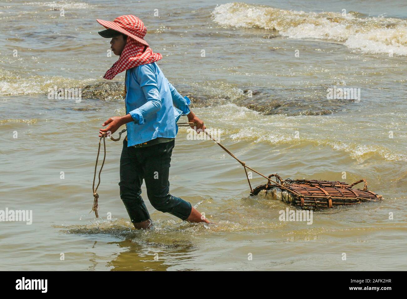 Fisherman in cappello di sole che tira un granchio cestino vicino al mercato del granchio in questo resort conosciuto per il suo pesce; Kep, provincia Di Kep, Cambogia Foto Stock