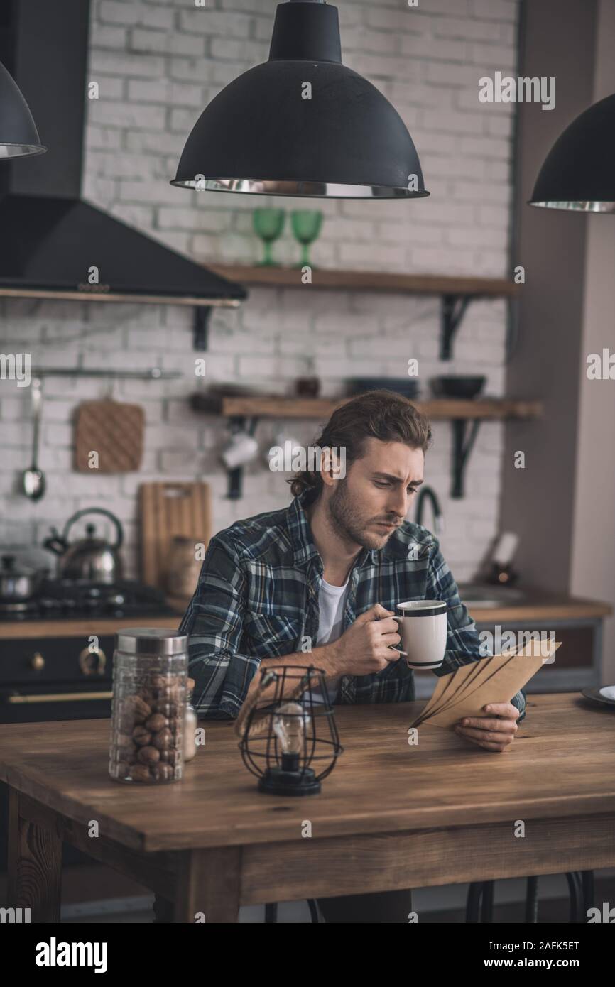 Giovane uomo bello leggere i vecchi lettere alla sua cucina Foto Stock