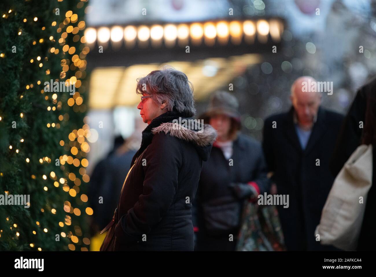 Capelli grigi lady guardando il Natale vetrina di Selfridges, iconico Selfridges entrata in background e passanti, London, Regno Unito Foto Stock