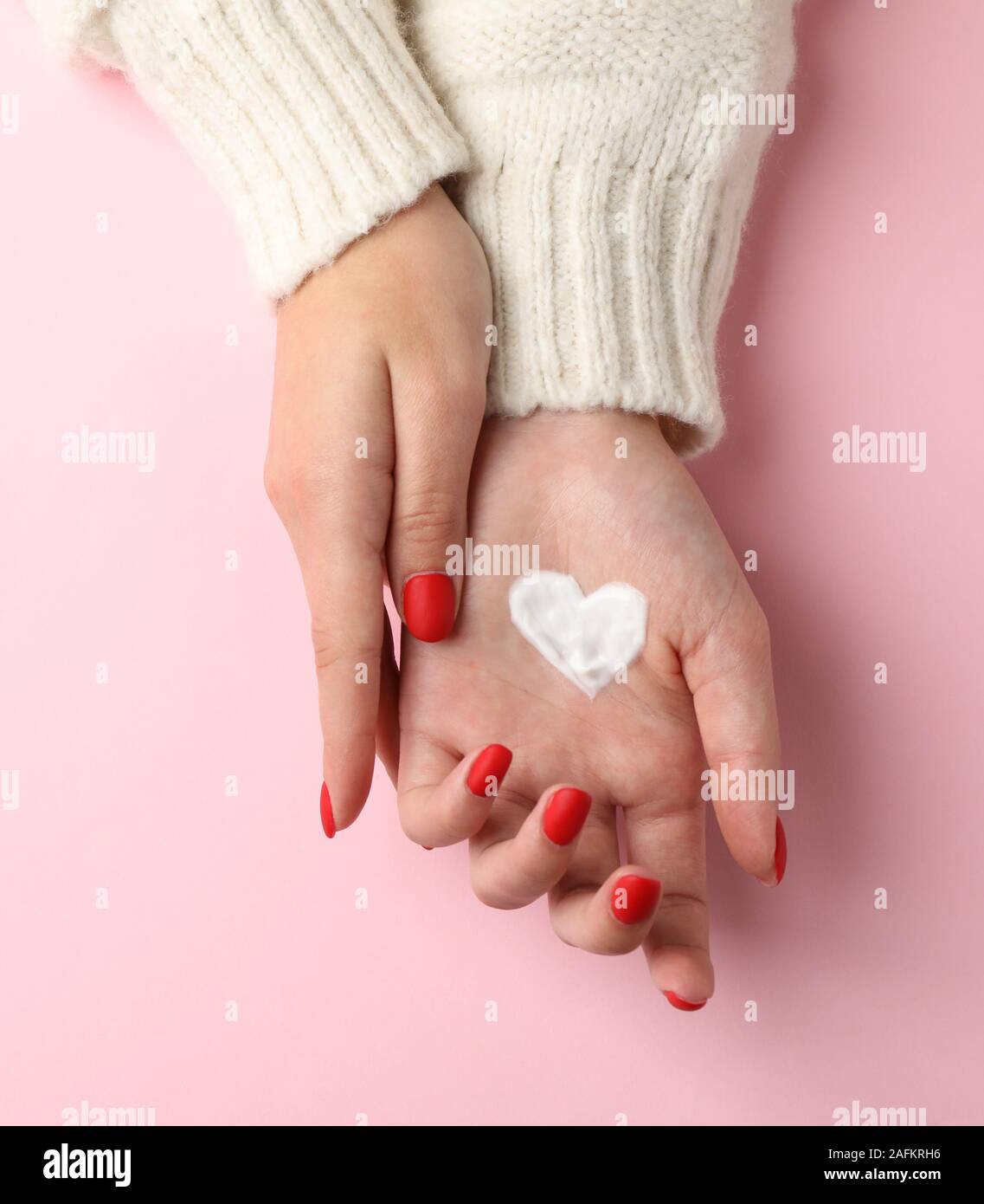 Donna mani, crema idratante per pulire e morbida la pelle in inverno, forma di cuore creato da crema su sfondo rosa, spazio per il testo. Vista dall'alto. H Foto Stock