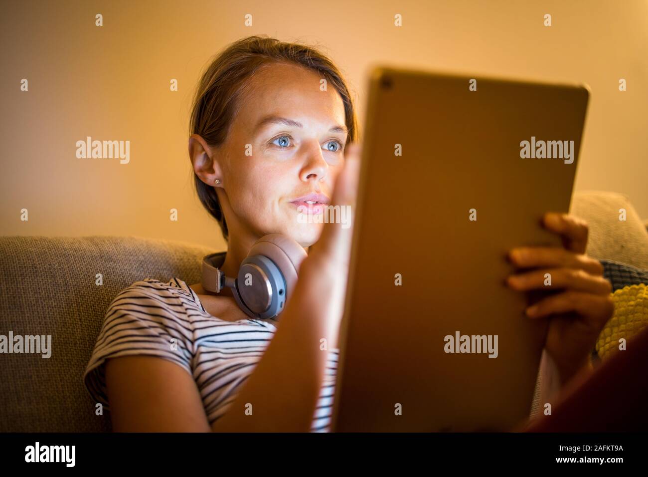 Piuttosto, giovane donna che lavorano a casa la sera - utilizzando il suo  tablet pc come pure delle cuffie bluetooth, scrivere alcune idee per domani  Foto stock - Alamy