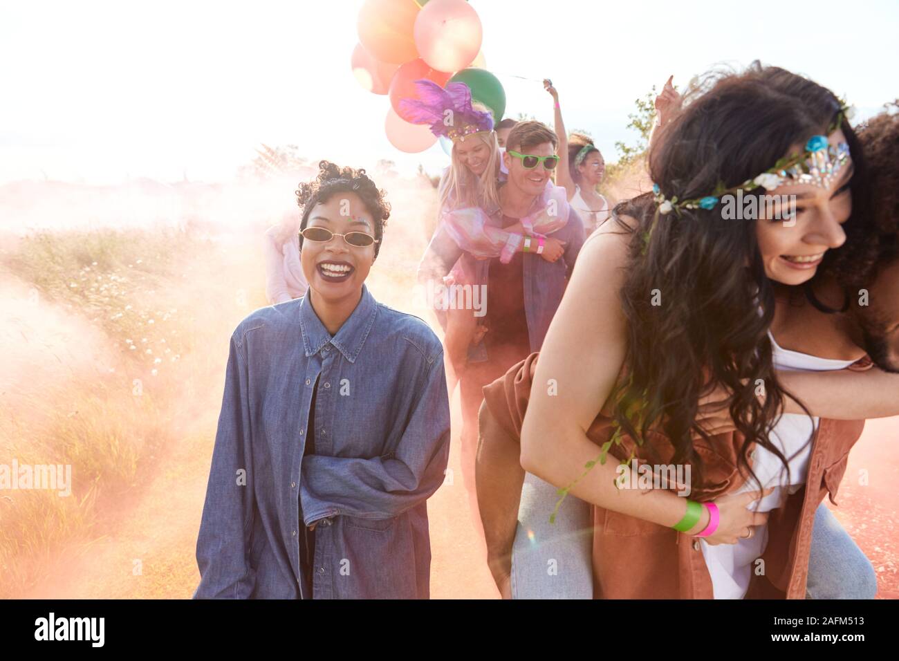 Gruppo di amici a piedi Torna alla tenda dopo aver aperto il Festival di musica con palloncini e fumo Flare Foto Stock