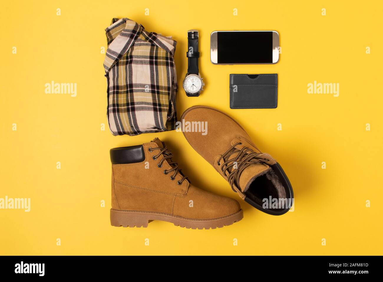 Layout di autunno vestiti e accessori in colori caldi su sfondo giallo. Shirt, stivali, telefono e guardare i laici piana nelle vicinanze. Foto Stock