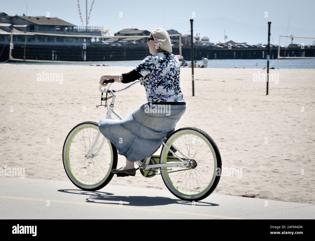 Tipo Hippie donna in berretto e Gonna Jeans grasso di equitazione stanco beach cruiser bicicletta lungo la pista ciclabile del Santa Barbara porto, Santa Barbara, CA. Foto Stock