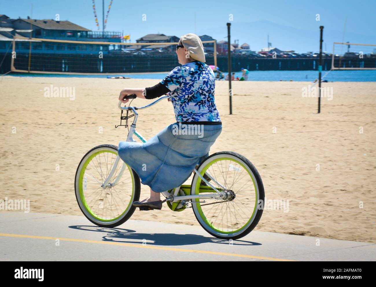 Tipo Hippie donna in berretto e Gonna Jeans grasso di equitazione stanco beach cruiser bicicletta lungo la pista ciclabile del Santa Barbara porto, Santa Barbara, CA. Foto Stock