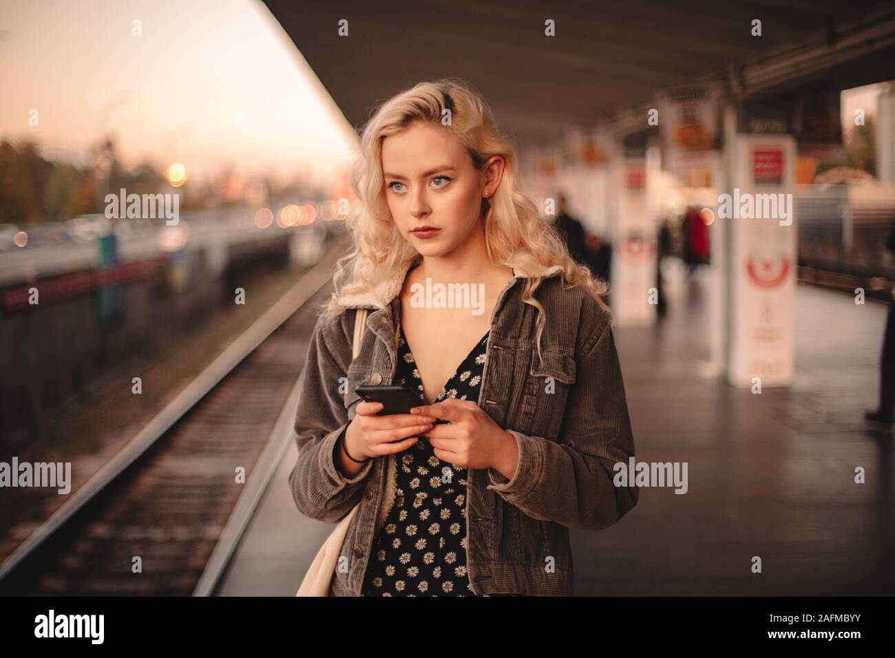 Giovane donna pensosa utilizzando smart phone durante l'attesa per il treno Foto Stock